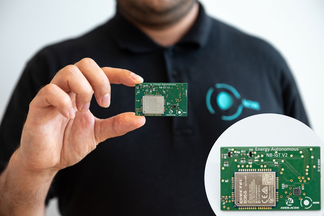 En person som håller ett litet grönt kretskort märkt 'Energy Autonomous NB-IoT V2' med en förstorad infälld bild som visar detaljer. Detta representerar energieffektiv hårdvara specifikt designad för blockkedje-IoT-applikationer, vilket direkt adresserar energiförbrukningsproblematiken hos blockkedjeteknik med autonoma strömlösningar.