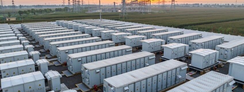 Stor batteripark med energilagringscontainrar intill elnätets kraftledningar