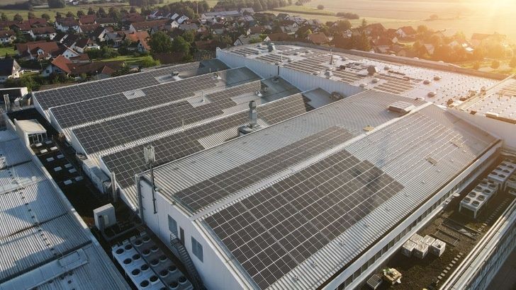Industribyggnad med stora solcellspaneler på taken nära ett bostadsområde