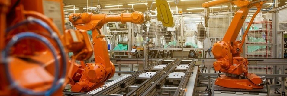 Orange industrirobotar arbetar vid transportbanor i en fabriksmiljö